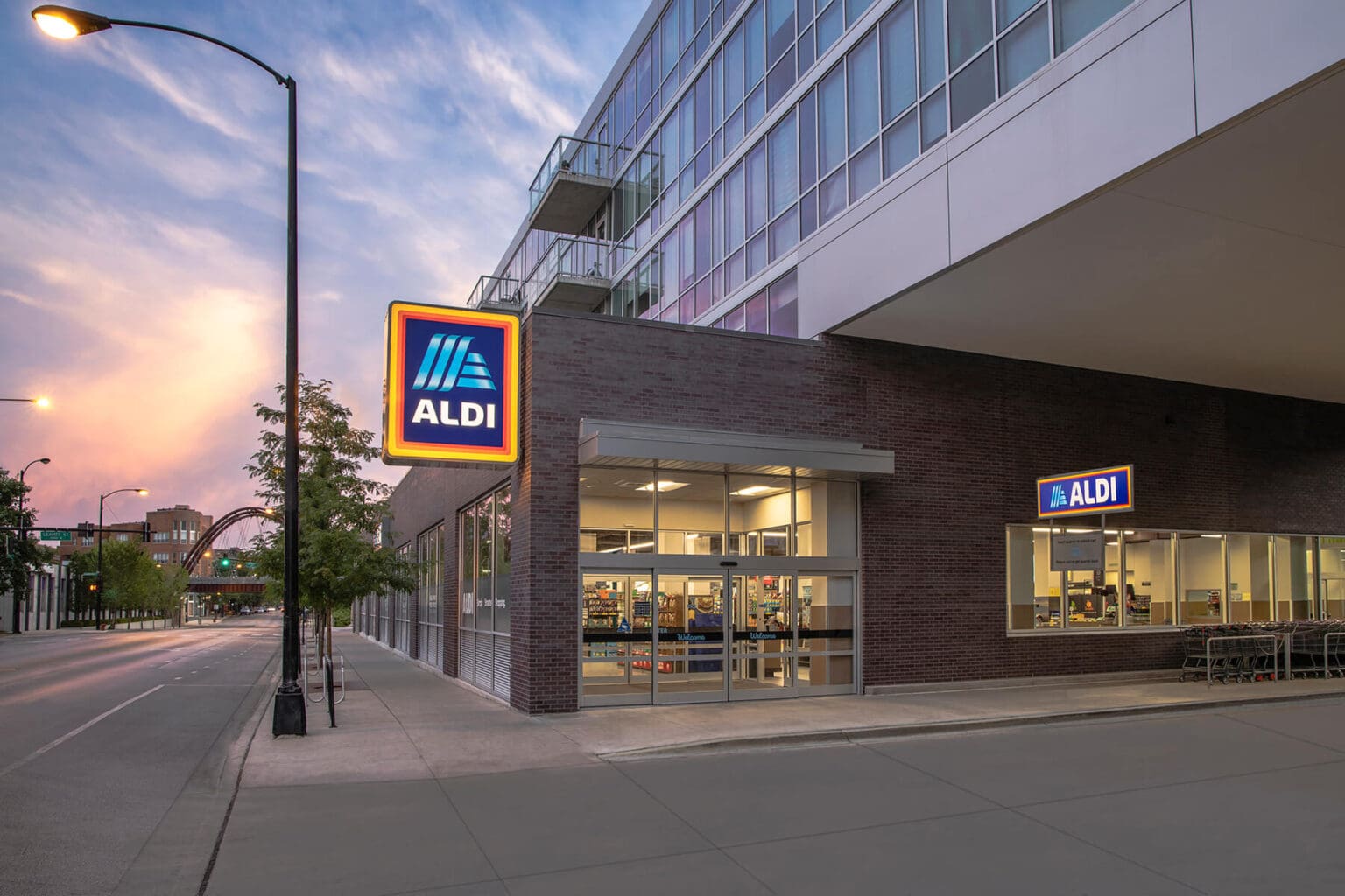 Exterior view of an Aldi store at sunset with entrance and sign visible.