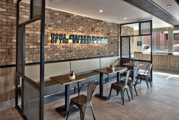 Modern Burger King interior with seating and Home of the Whopper sign on a brick wall.