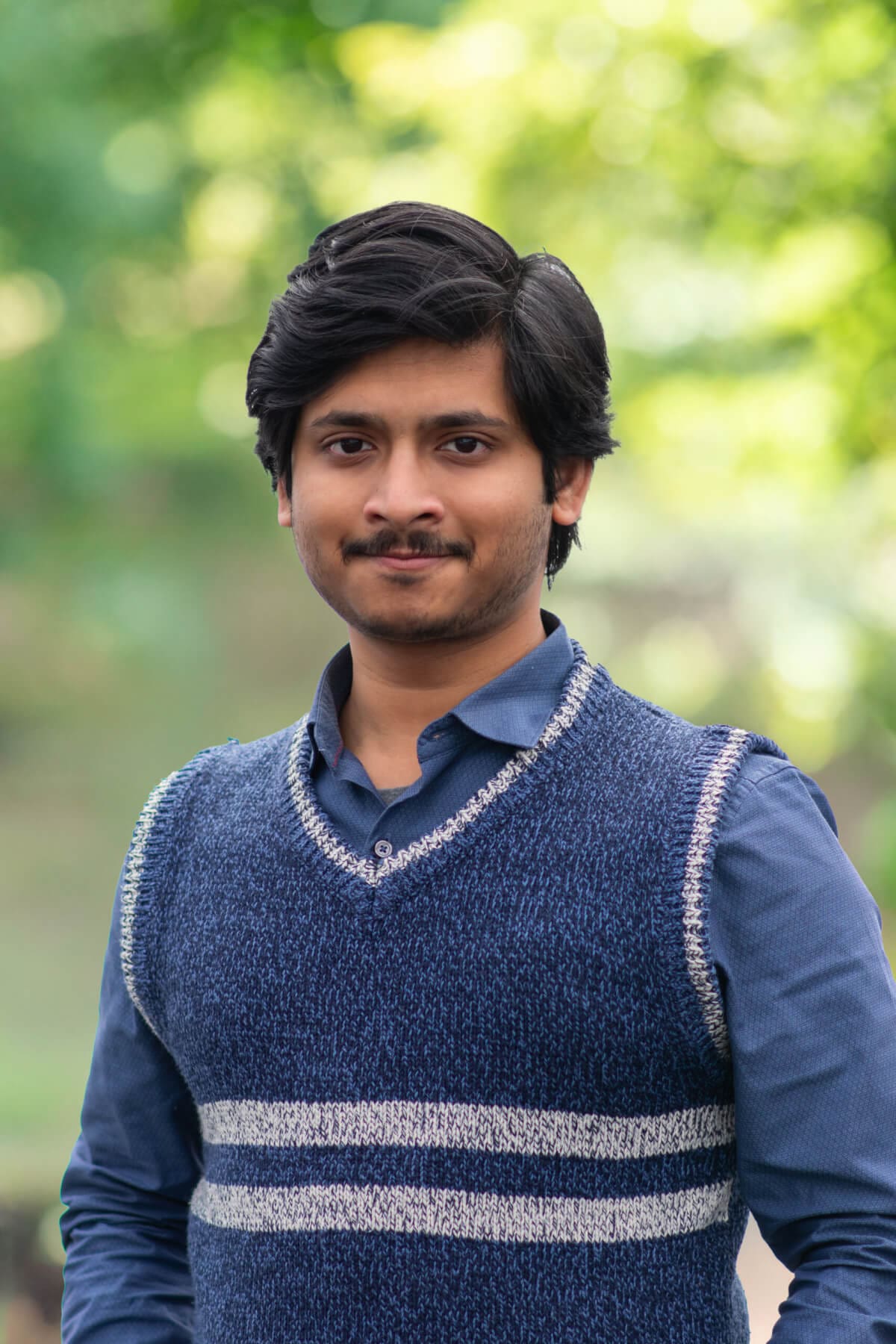 Professional headshot of man standing outdoors with a blurred green background.