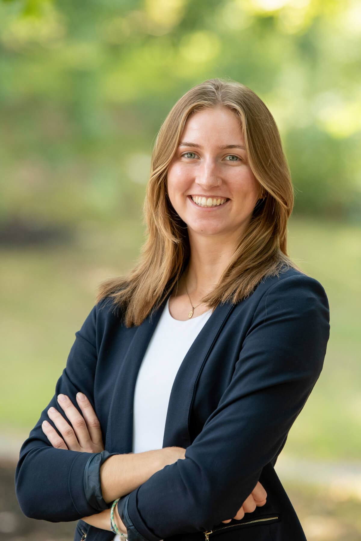 Professional headshot of woman standing outdoors with a blurred green background.