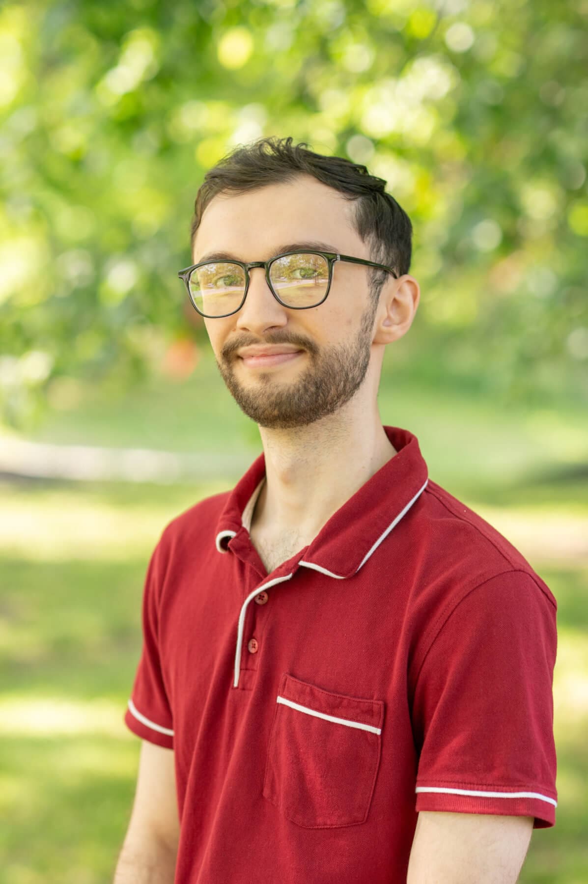 Professional headshot of man standing outdoors with a blurred green background.