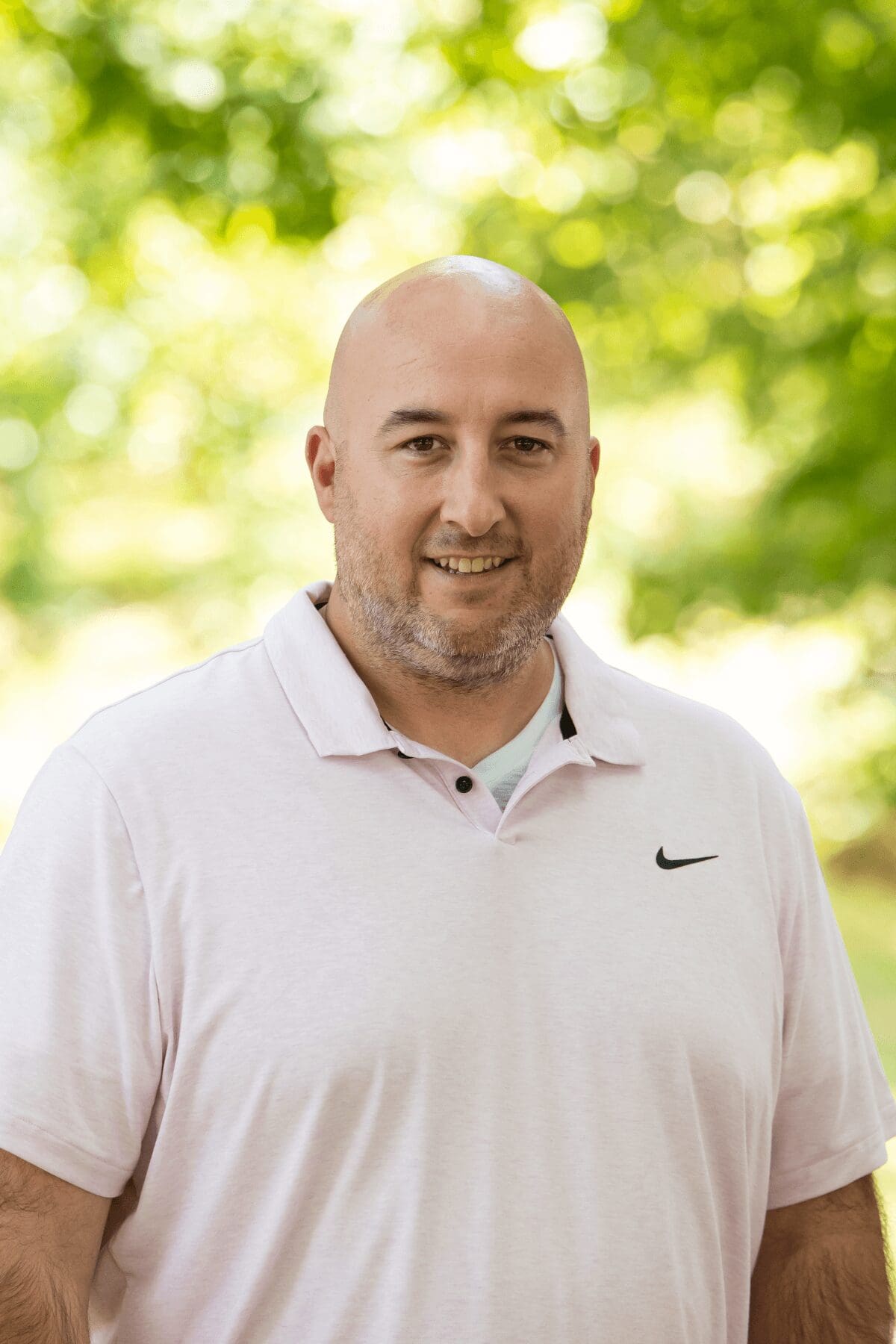 Professional headshot of man standing outdoors with a blurred green background.