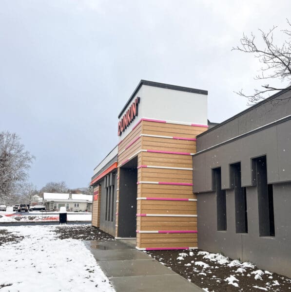 Modern Dunkin' store exterior on a snowy day, featuring brand colors.