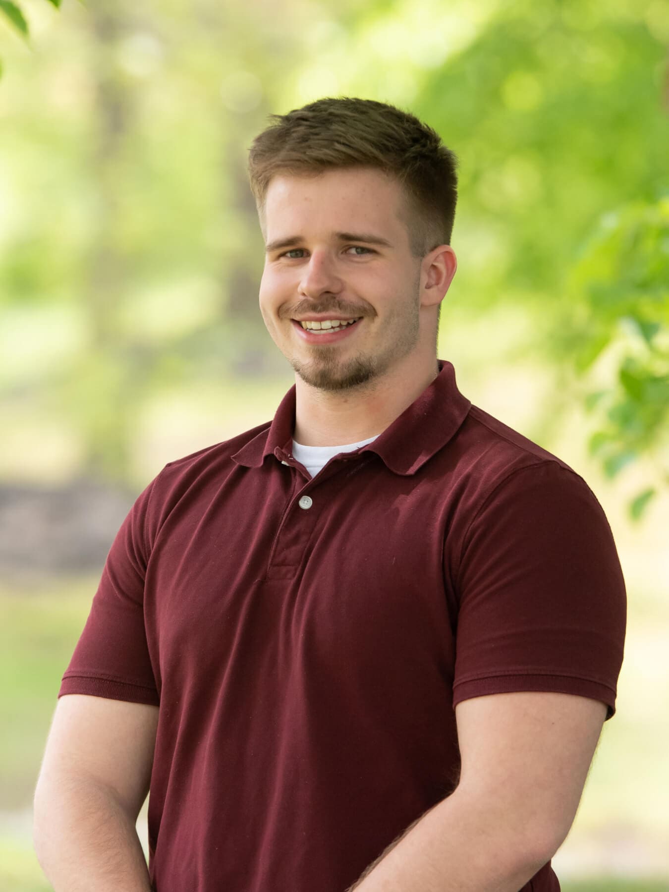 Professional headshot of man standing outdoors with a blurred green background.
