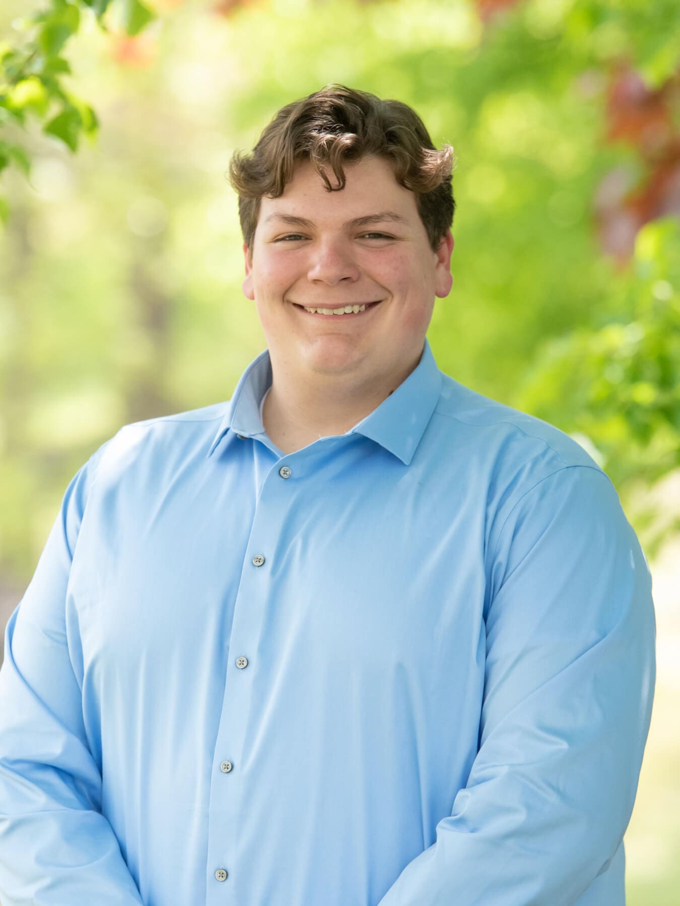 Professional headshot of man standing outdoors with a blurred green background.