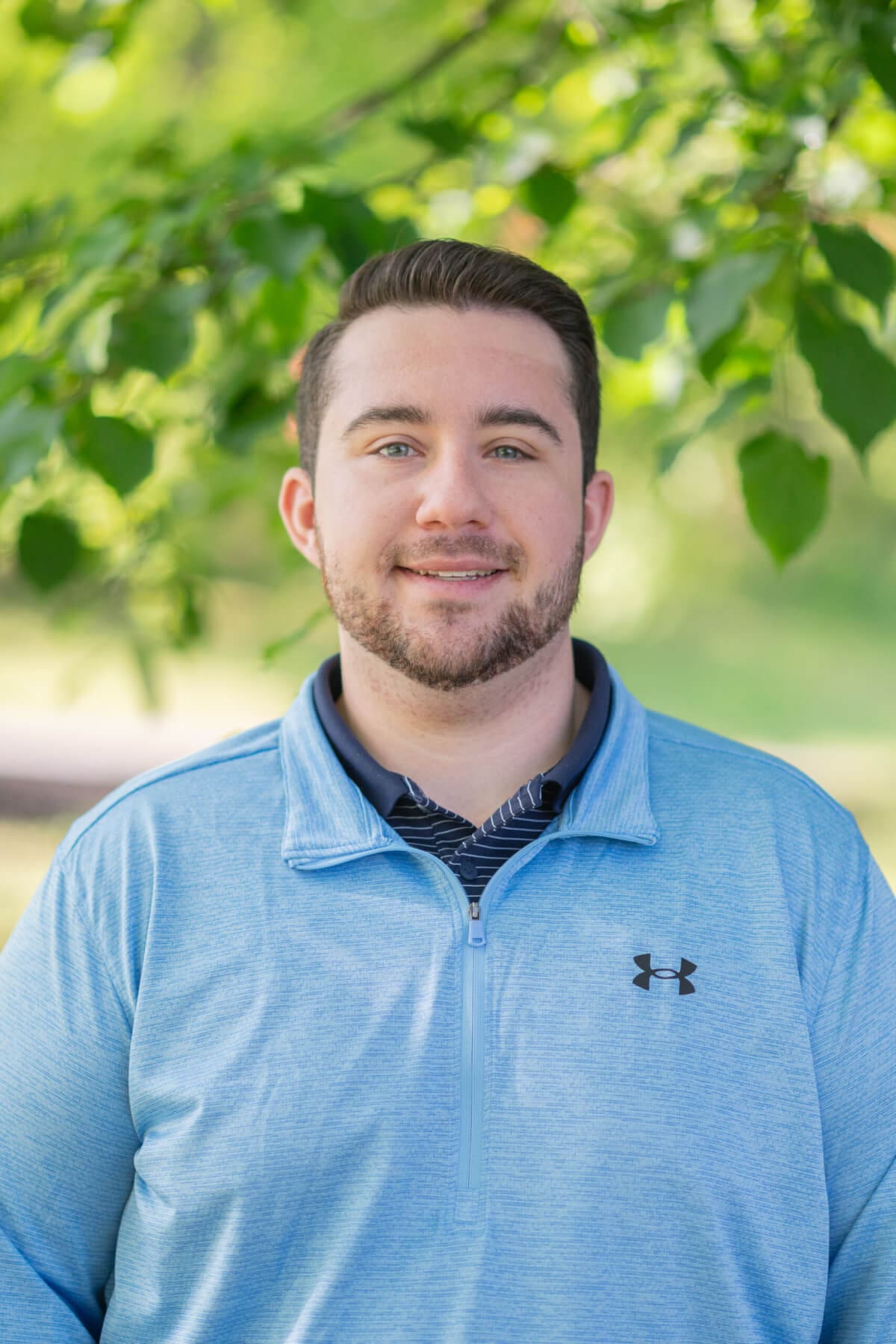 Professional headshot of man standing outdoors with a blurred green background.
