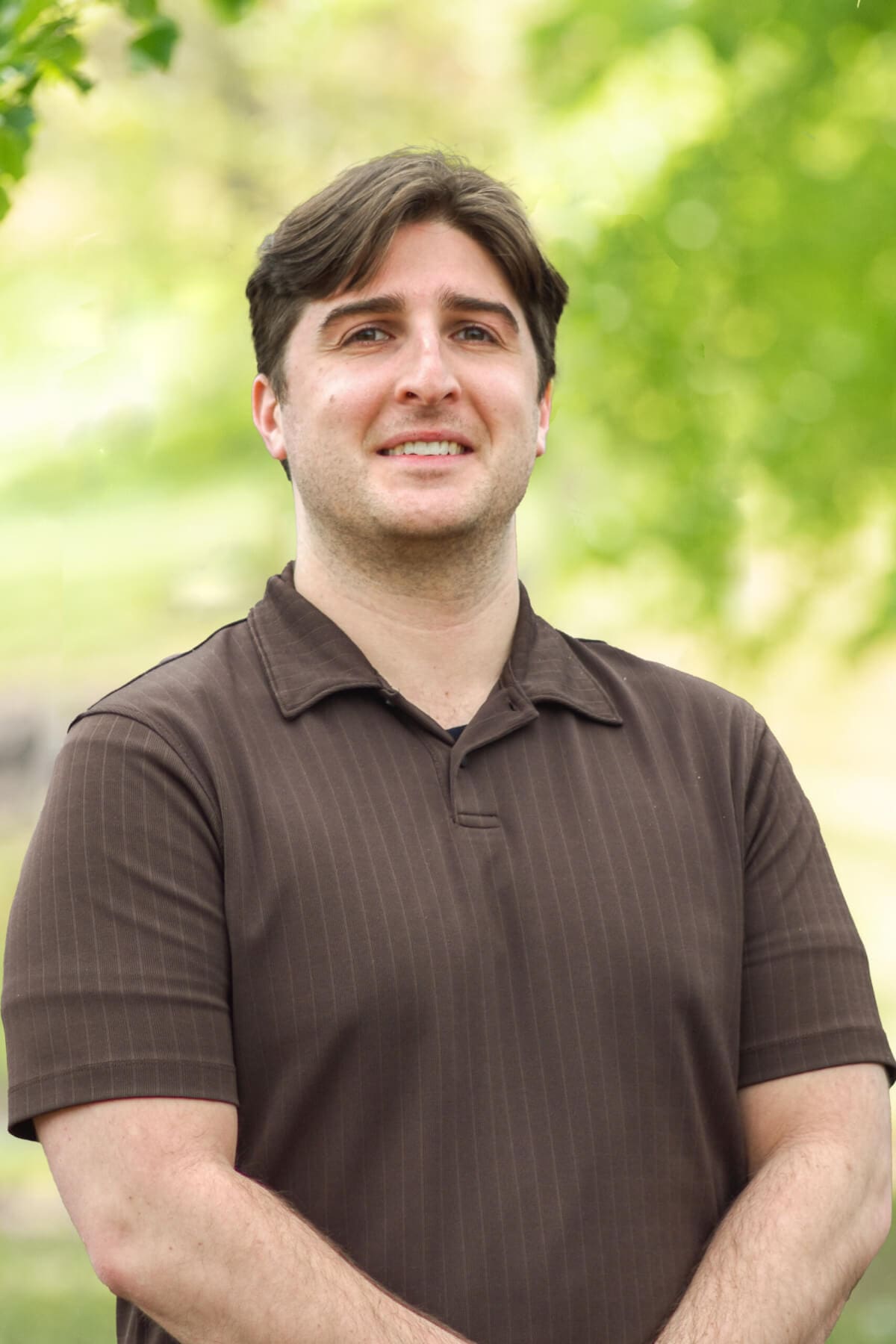 Professional headshot of man standing outdoors with a blurred green background.
