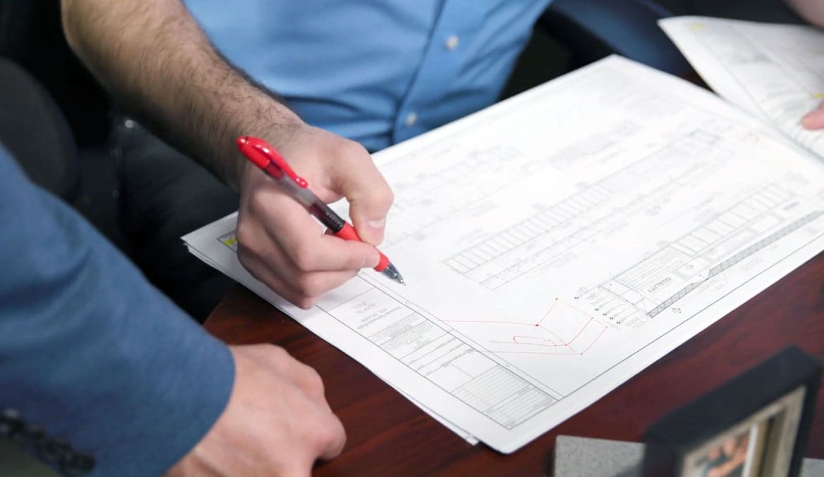 Architect reviewing blueprints at a desk with a red pen, focusing on design details.