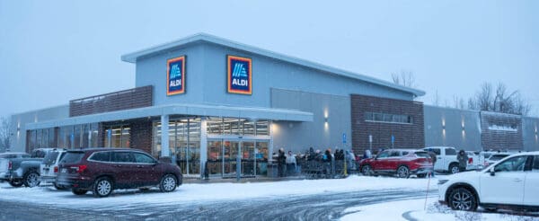 Snowy Aldi storefront with parked cars and shoppers, highlighting convenient grocery shopping in winter conditions.