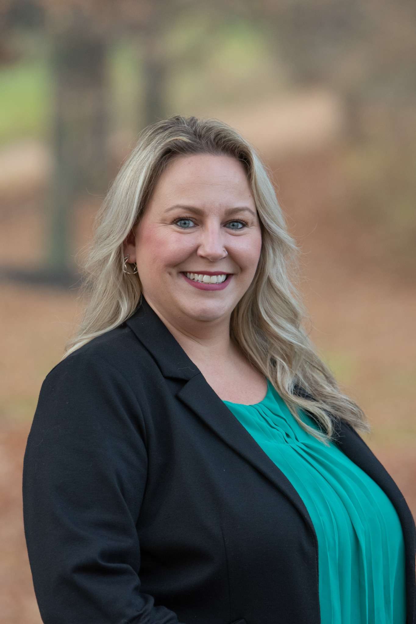 Professional headshot of woman standing outdoors with a blurred brown background.