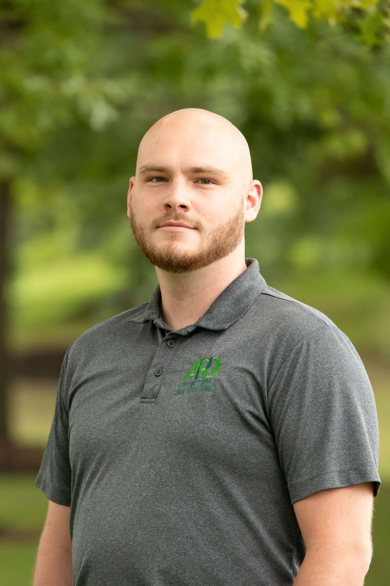 Professional headshot of man standing outdoors with a blurred green background.