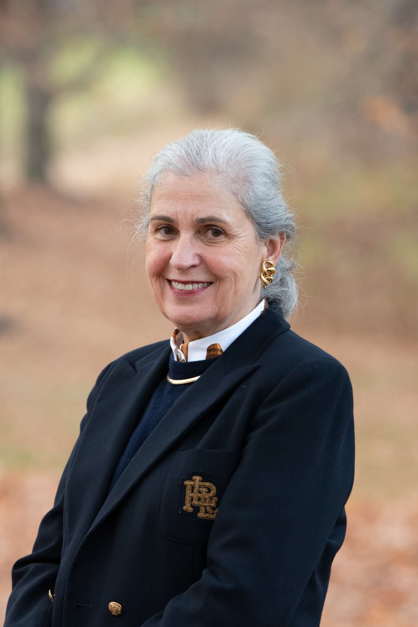 Professional headshot of woman standing outdoors with a blurred brown background.