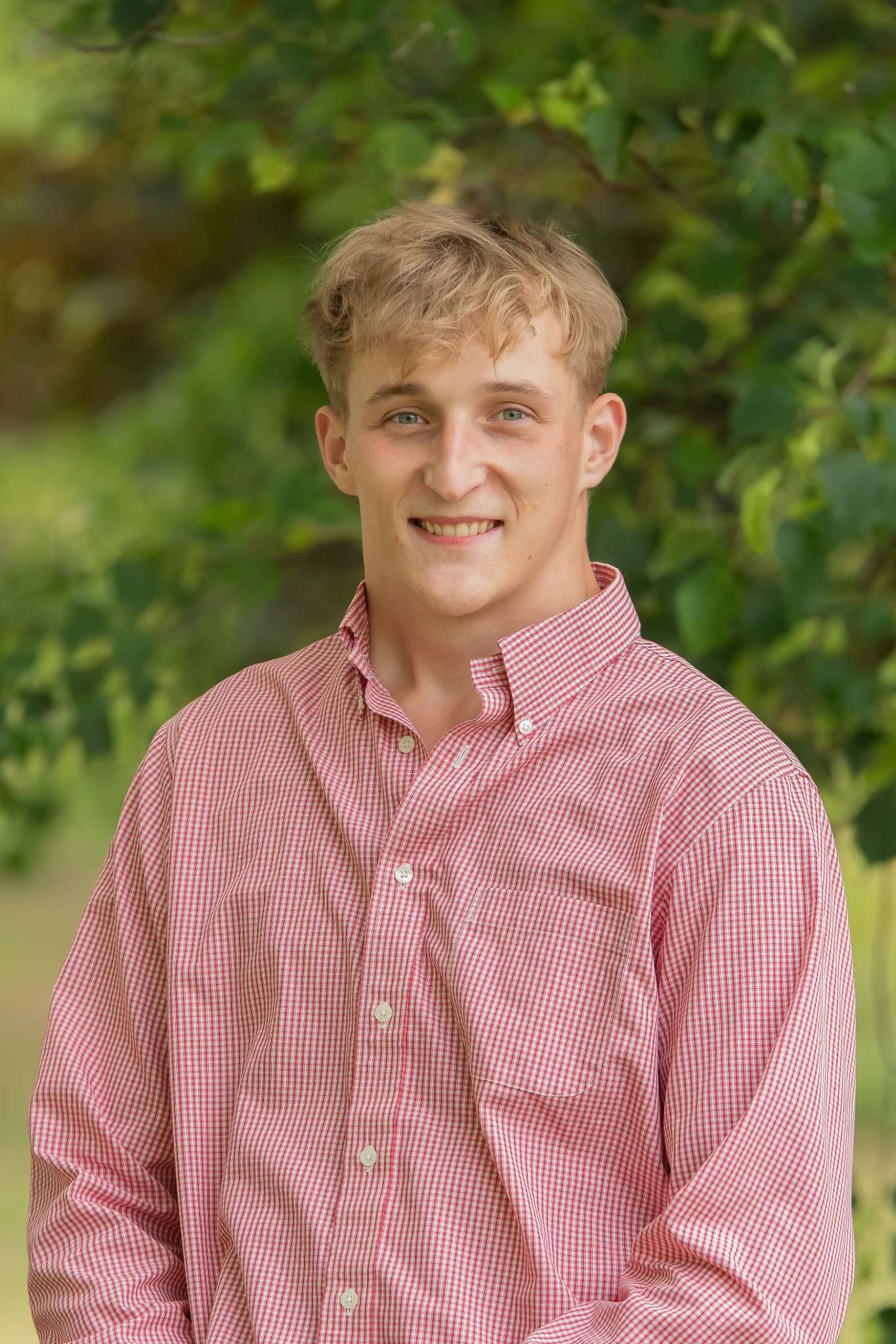 Professional headshot of man standing outdoors with a blurred green background.