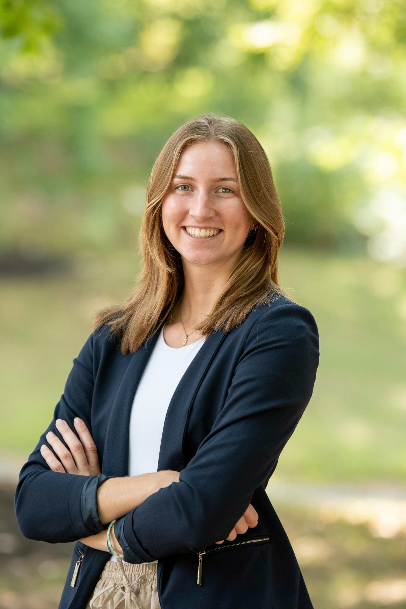 Professional headshot of woman standing outdoors with a blurred green background.
