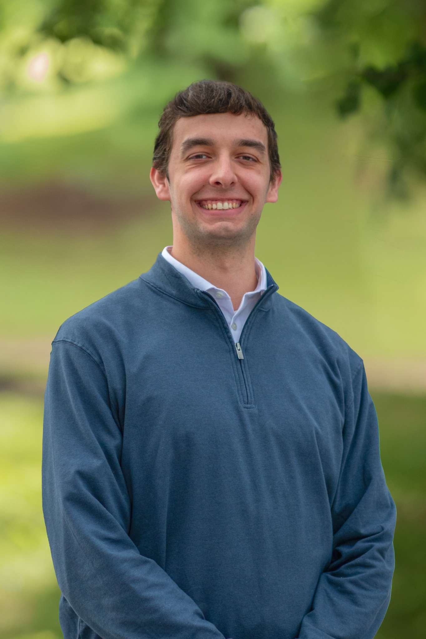 Professional headshot of man standing outdoors with a blurred green background.