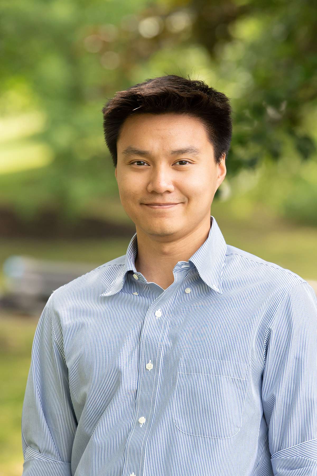 Professional headshot of man standing outdoors with a blurred green background.