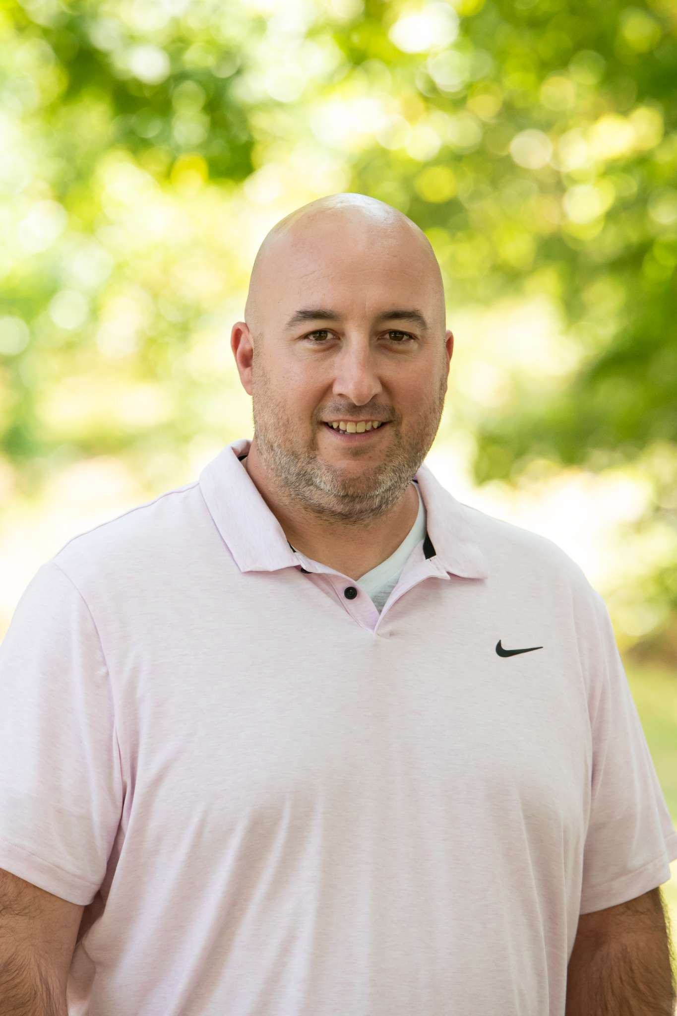 Professional headshot of man standing outdoors with a blurred green background.