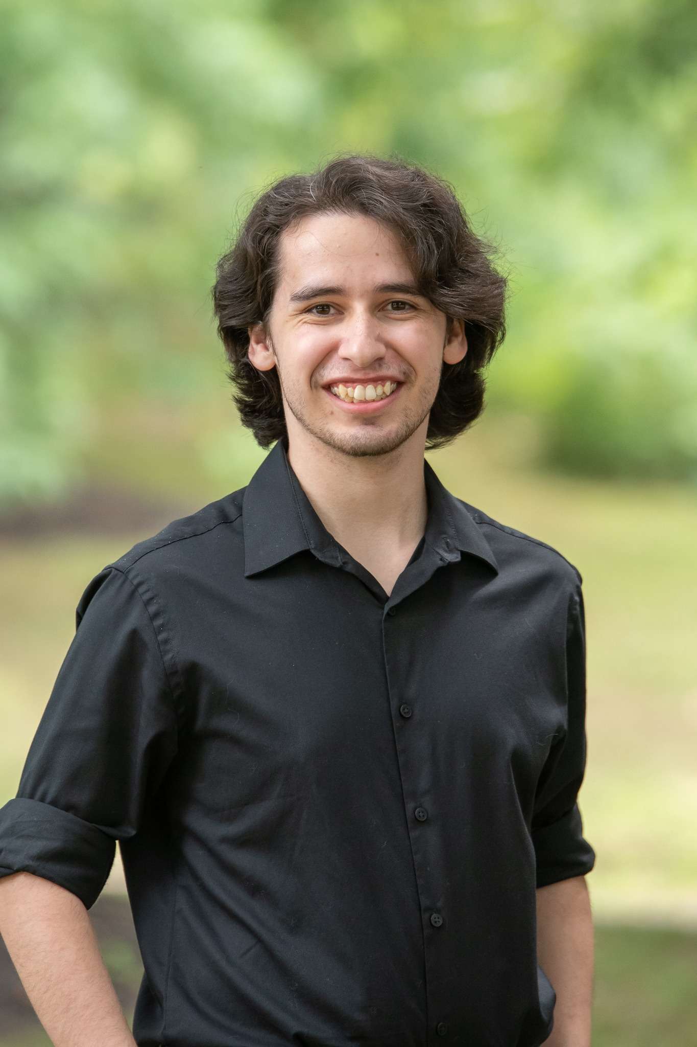 Professional headshot of man standing outdoors with a blurred green background.
