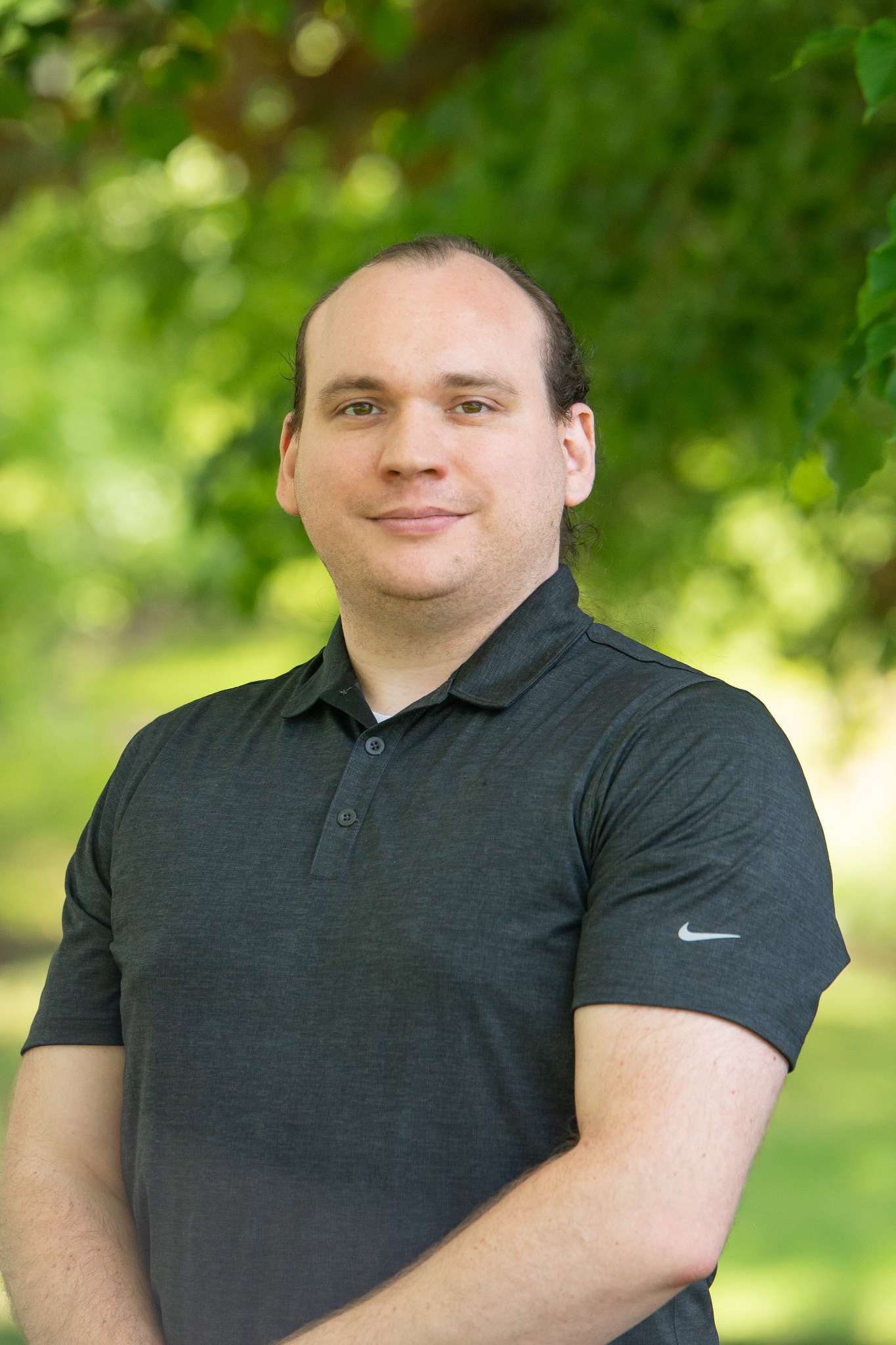 Professional headshot of man standing outdoors with a blurred green background.