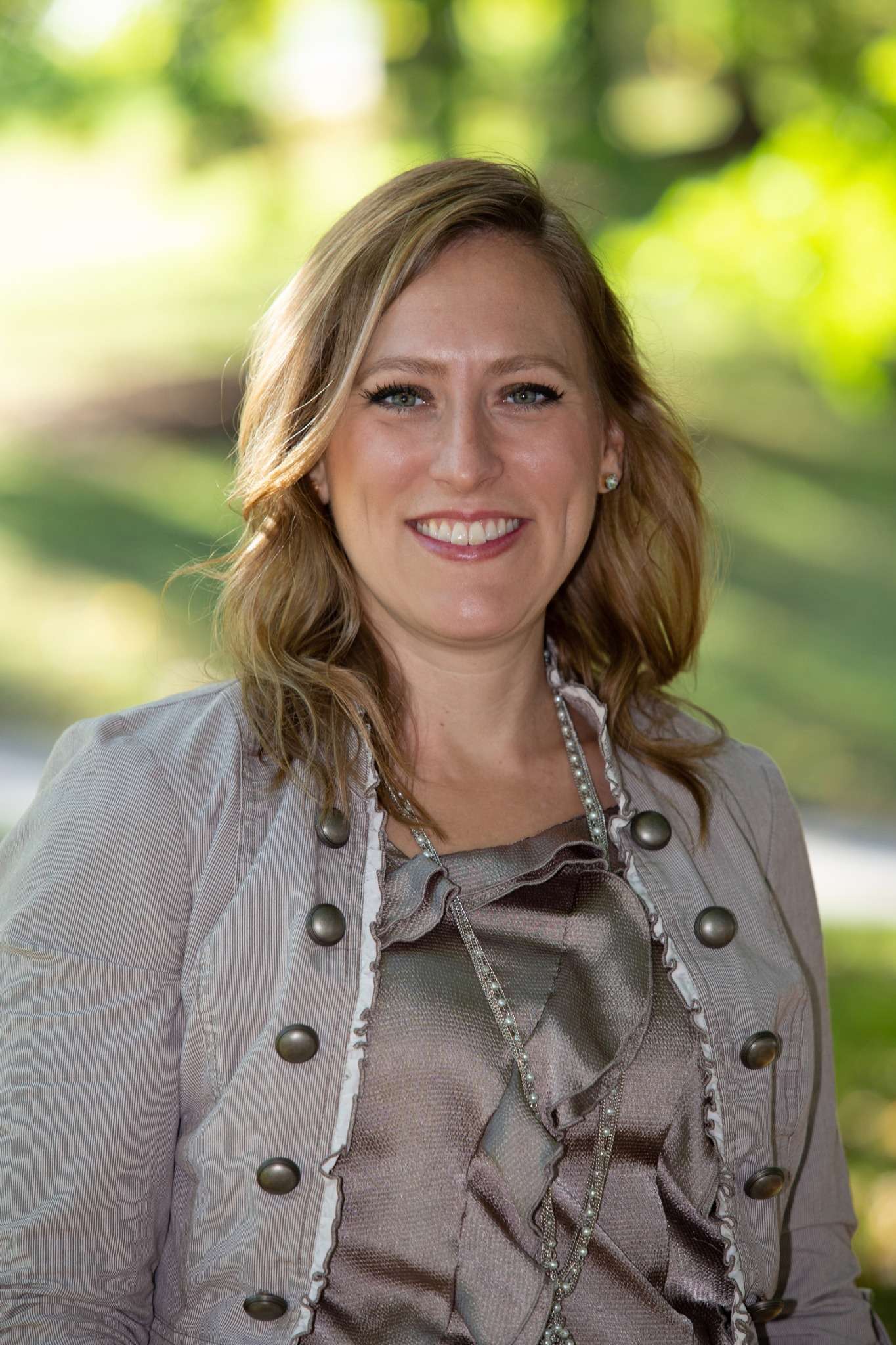 Professional headshot of woman standing outdoors with a blurred green background.
