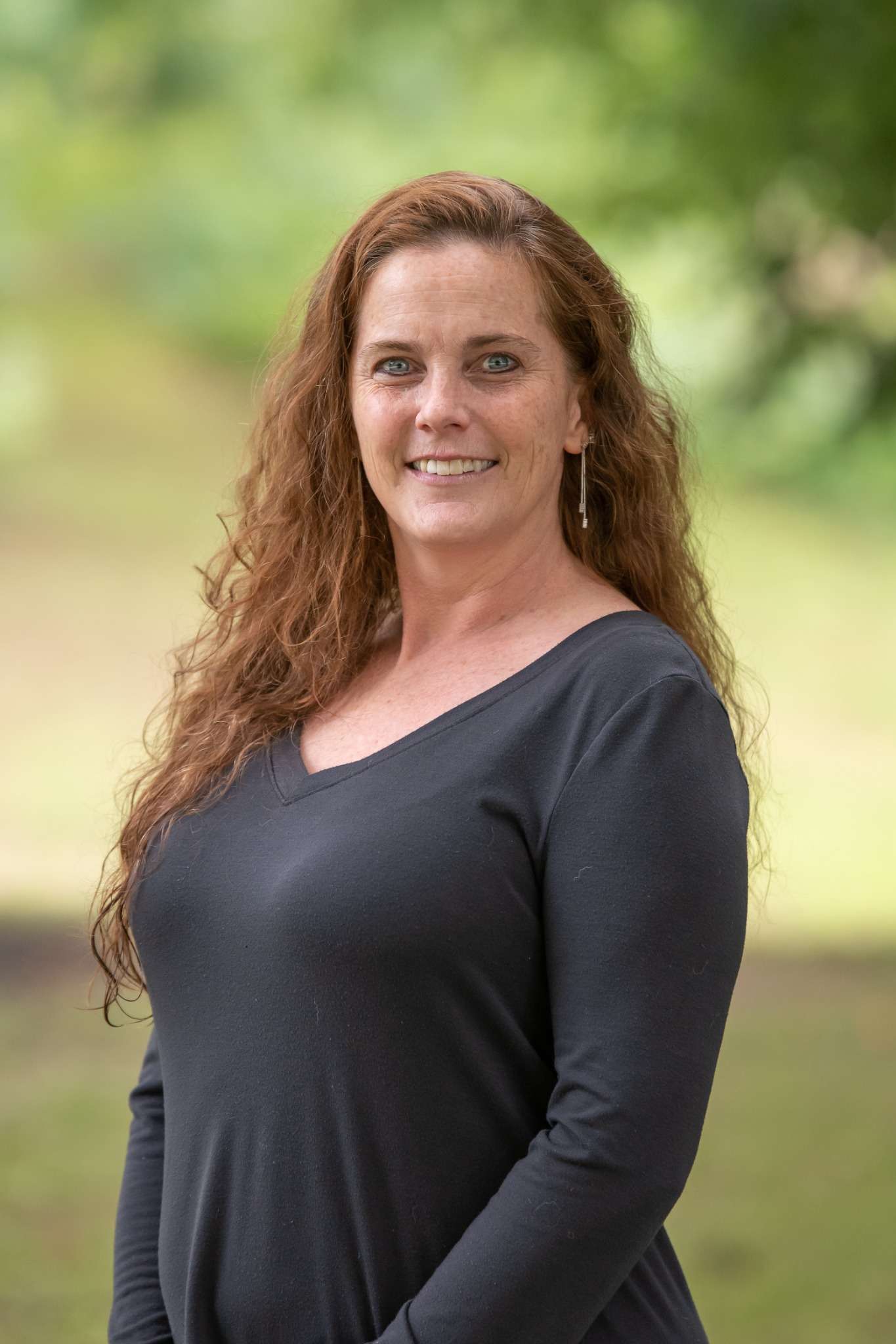 Professional headshot of woman standing outdoors with a blurred green background.