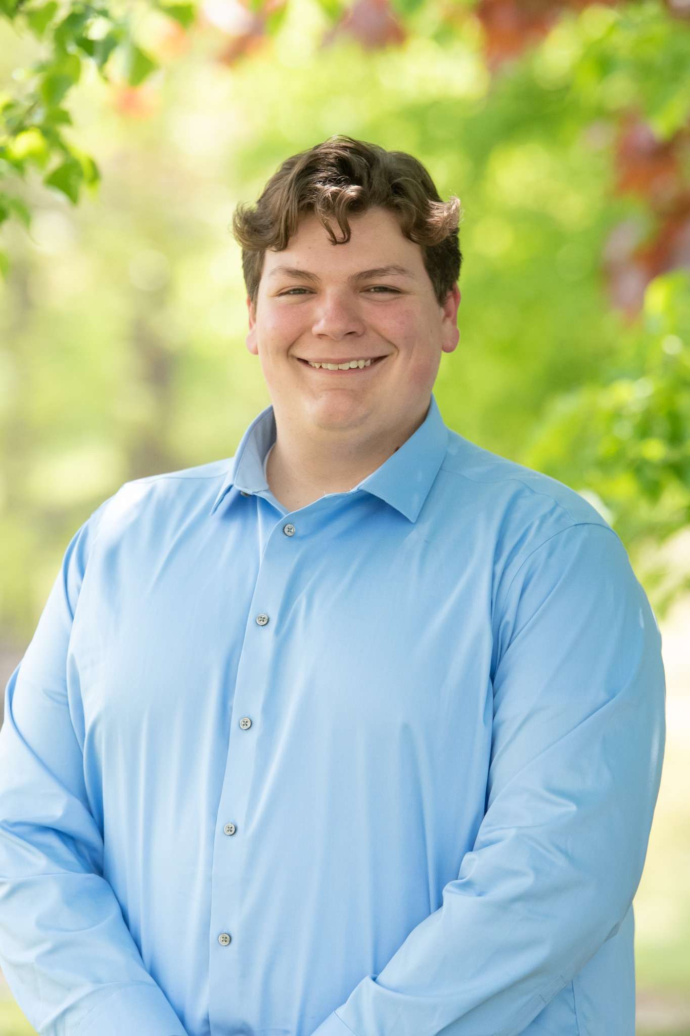 Professional headshot of man standing outdoors with a blurred green background.