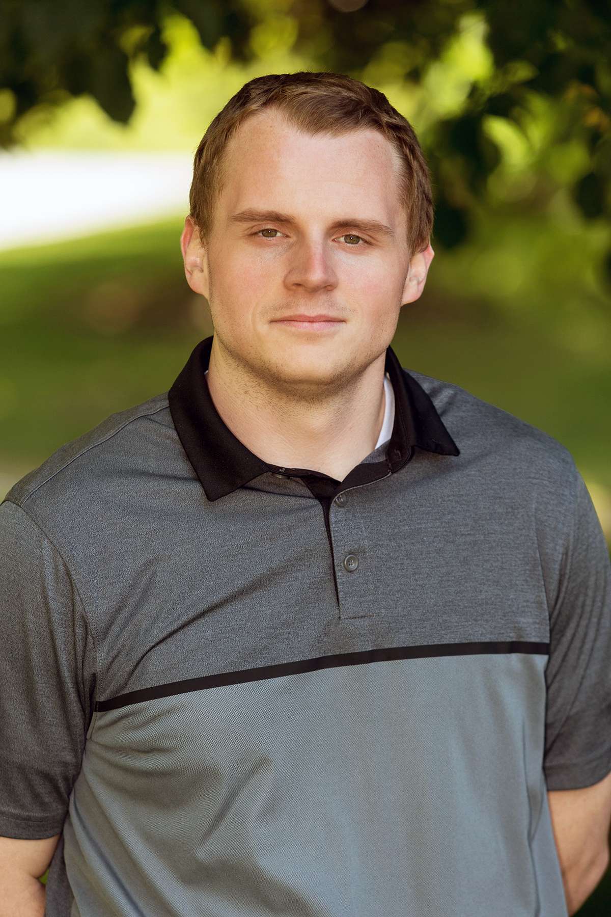 Professional headshot of man standing outdoors with a blurred green background.