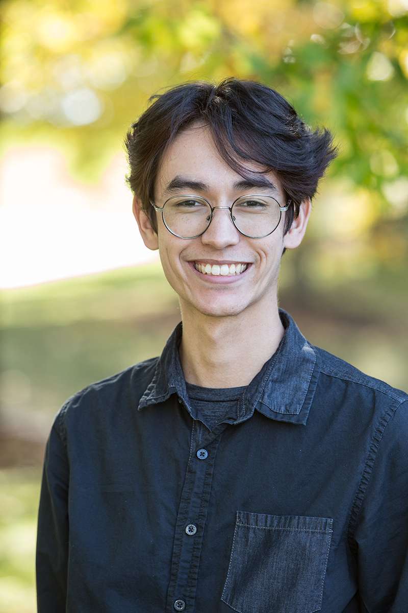 Professional headshot of man standing outdoors with a blurred green background.