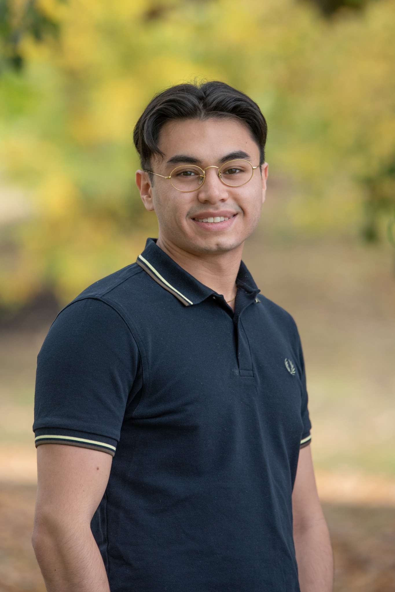 Professional headshot of man standing outdoors with a blurred green background.