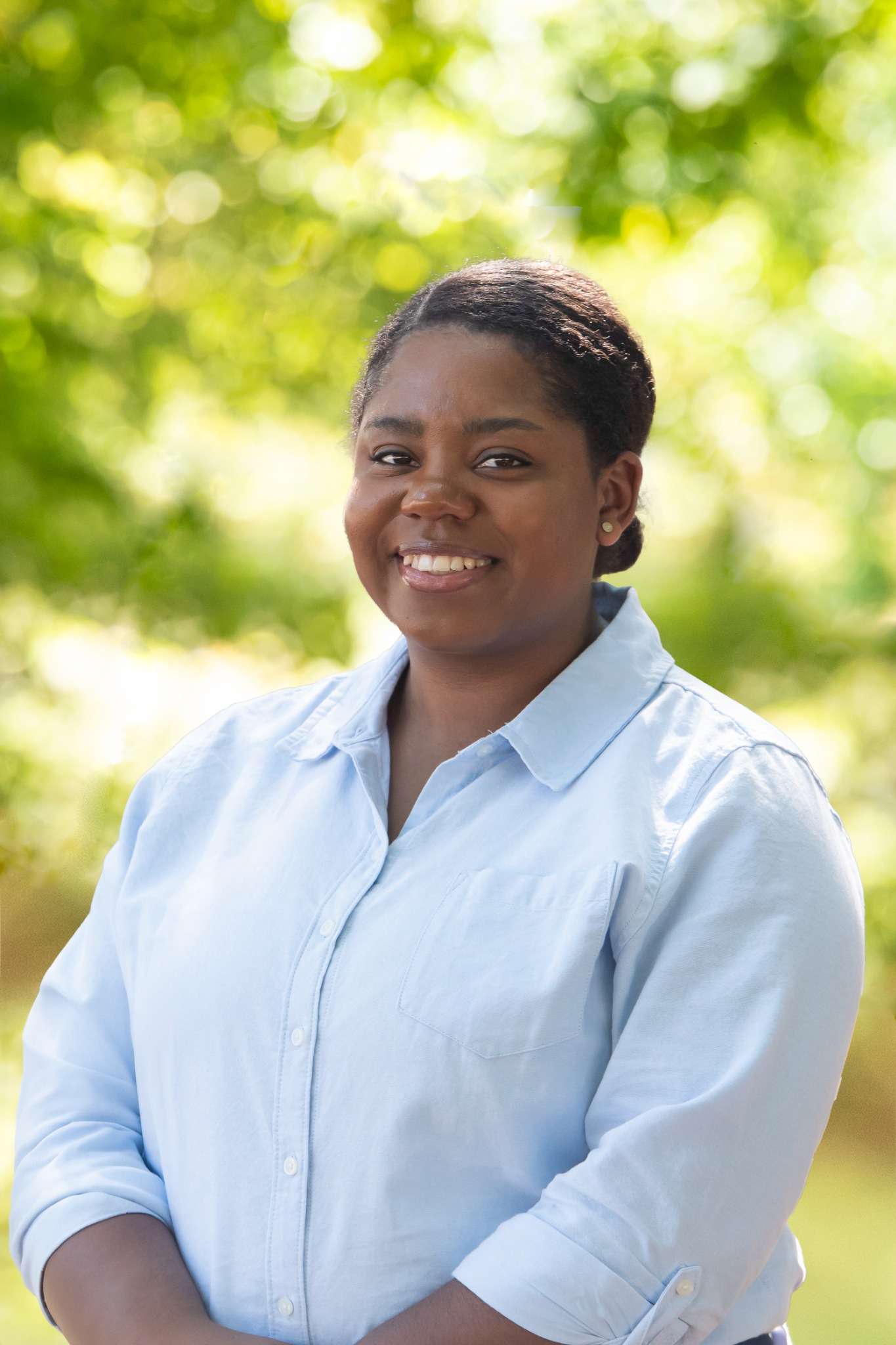 Professional headshot of woman standing outdoors with a blurred green background.