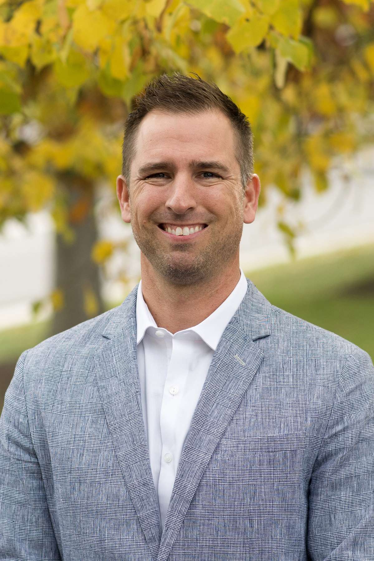 Professional headshot of man standing outdoors with a blurred green background.
