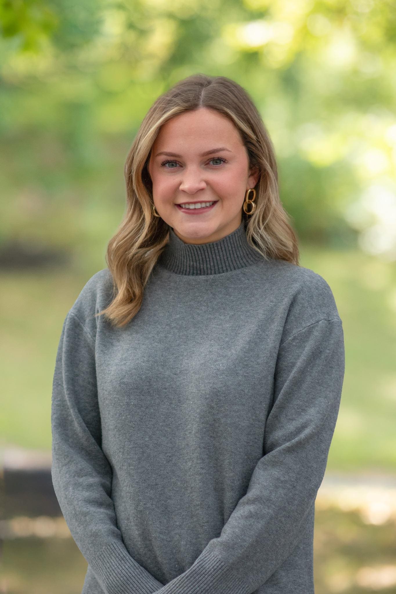 Professional headshot of woman standing outdoors with a blurred green background.