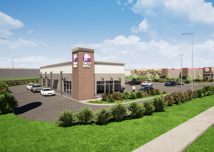 Modern Taco Bell drive-thru with cars in line, showcasing new design and landscaping against a clear blue sky.