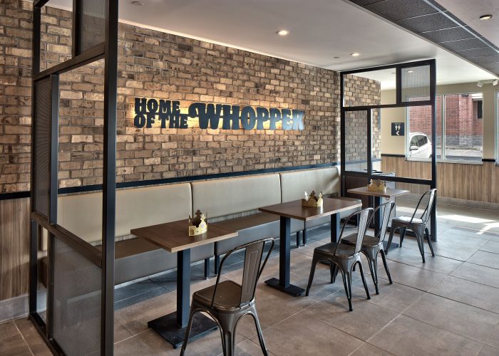 Burger King dining area with Home of the Whopper sign on brick wall. Cozy seating with crowns on tables.