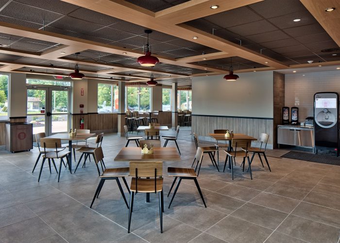Spacious fast-food restaurant interior with wooden tables and chairs, natural light streaming through large windows.