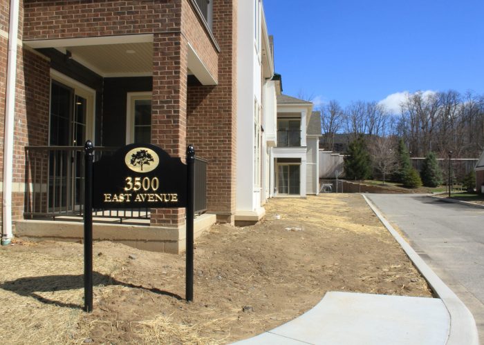 Sign displaying 3500 East Avenue in front of a brick building under clear blue sky.