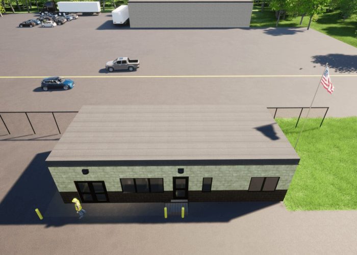 Aerial view of a small warehouse building with parking lot, trucks, and American flag nearby.