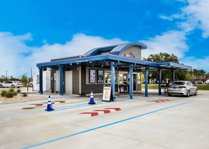 Drive-thru coffee shop with a silver car at Seven Brew, featuring modern design and clear blue sky.