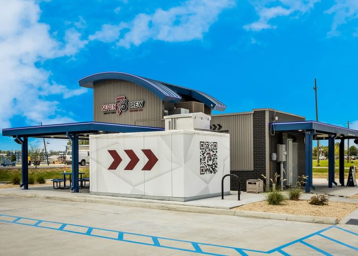 Drive-thru coffee stand with branding and QR code at Seven Brew under a clear blue sky.