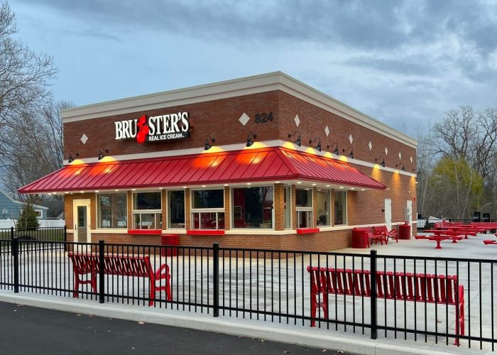 Brick ice cream shop with a red roof and outdoor seating at dusk.