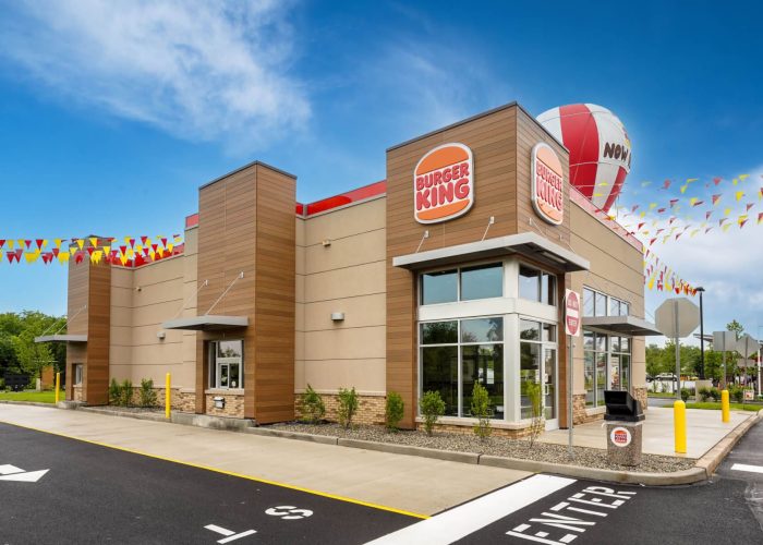 Exterior view of a Burger King restaurant on a clear day, featuring bold signage and festive flags.