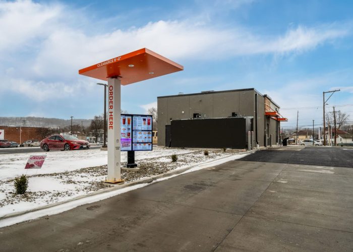 Drive-thru menu board at a fast-food restaurant on a snowy day, with a red car in line.