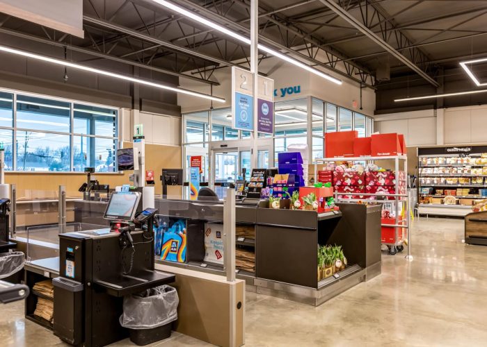 Modern grocery store checkout area with self-service kiosks and product displays.
