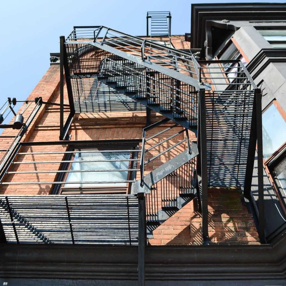 Industrial spiral fire escape on a brick building, casting shadows in sunlight.