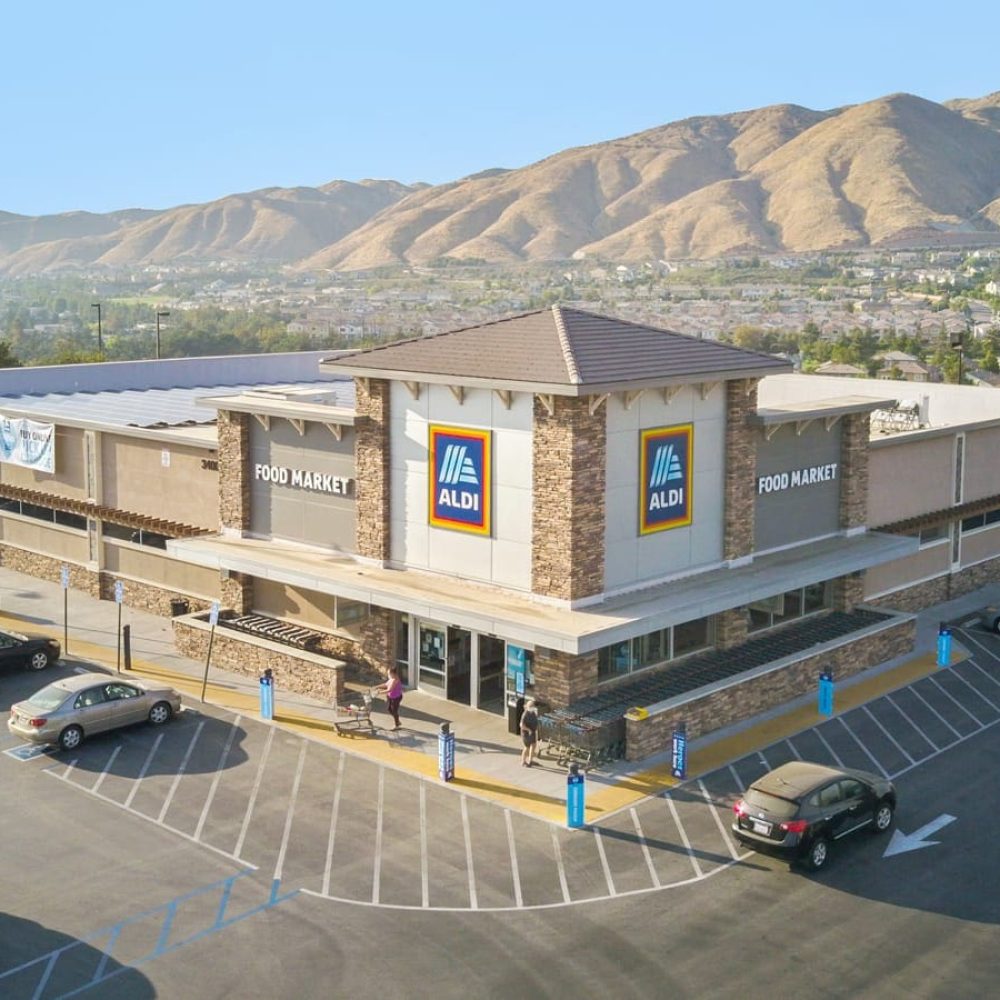 Aldi supermarket exterior with a mountainous backdrop, showcasing ample parking space on a sunny day.