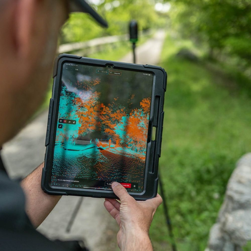 Person using tablet with LiDAR scanning on forest path.