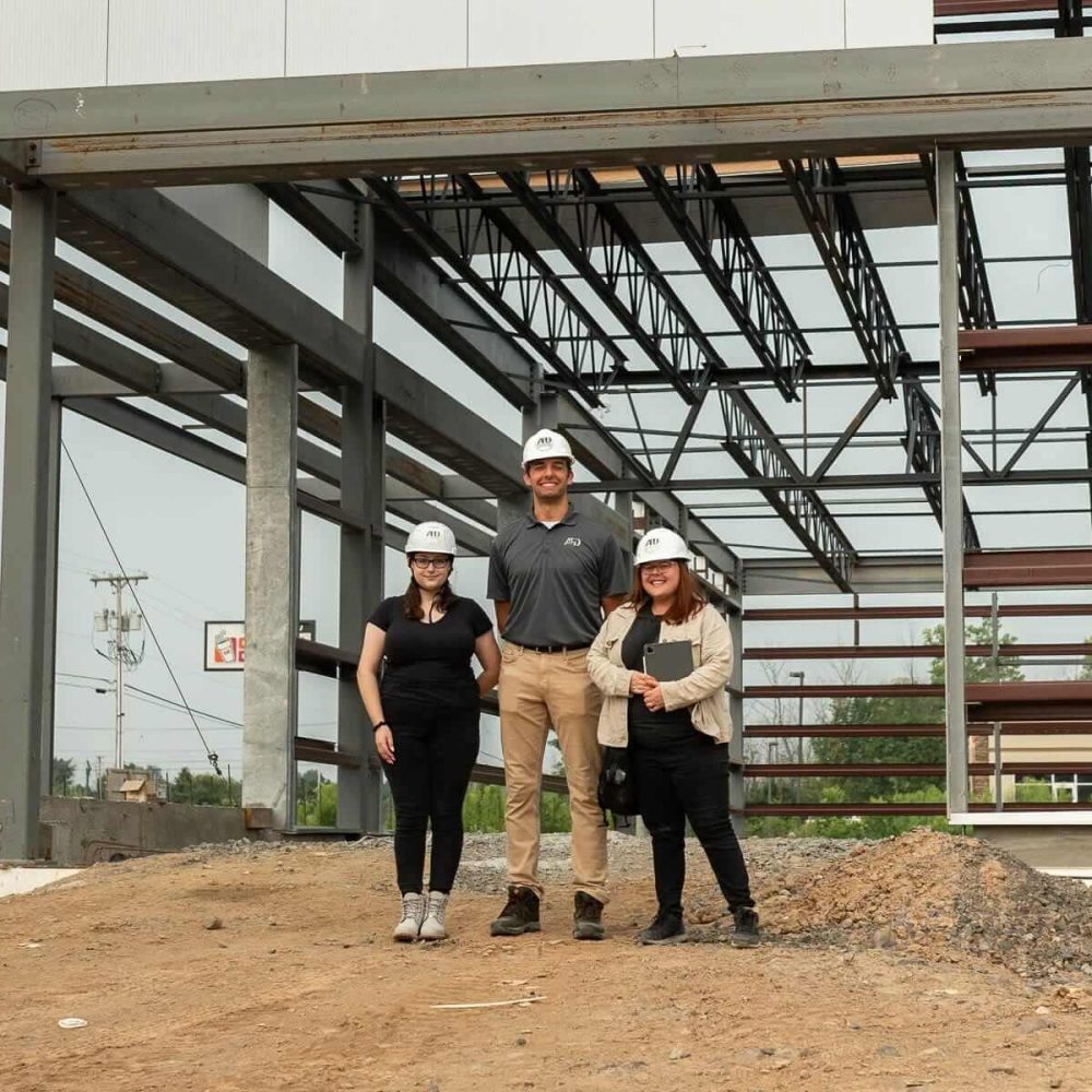 Construction team at a building site under steel framework, wearing hard hats.