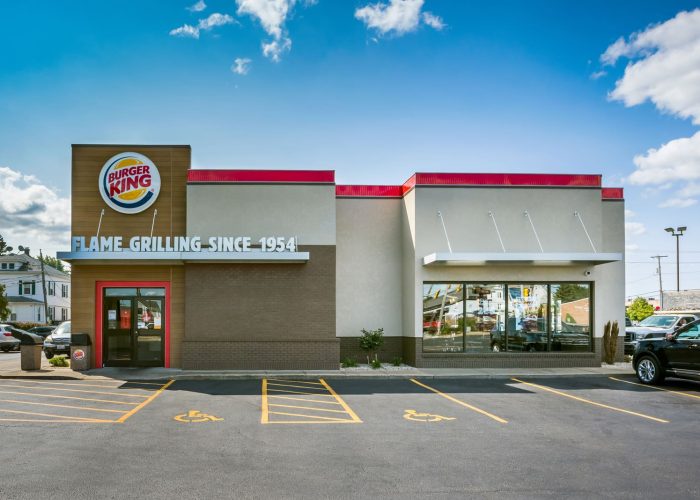 Burger King restaurant exterior showcasing classic flame-grilling sign under a clear blue sky.