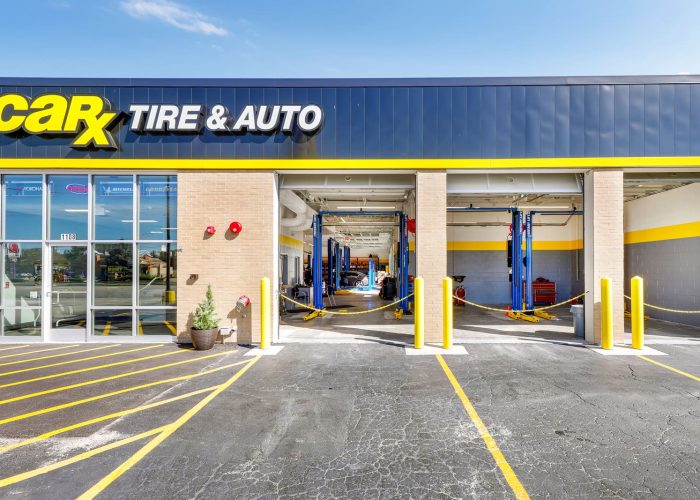CarX Tire & Auto service center exterior with open garage bays, bright signage, and clear sky.