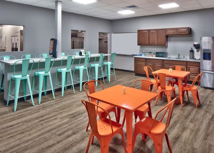 Modern breakroom with orange tables and teal stools, ideal for office relaxation. Perfect for enhancing workspace comfort.